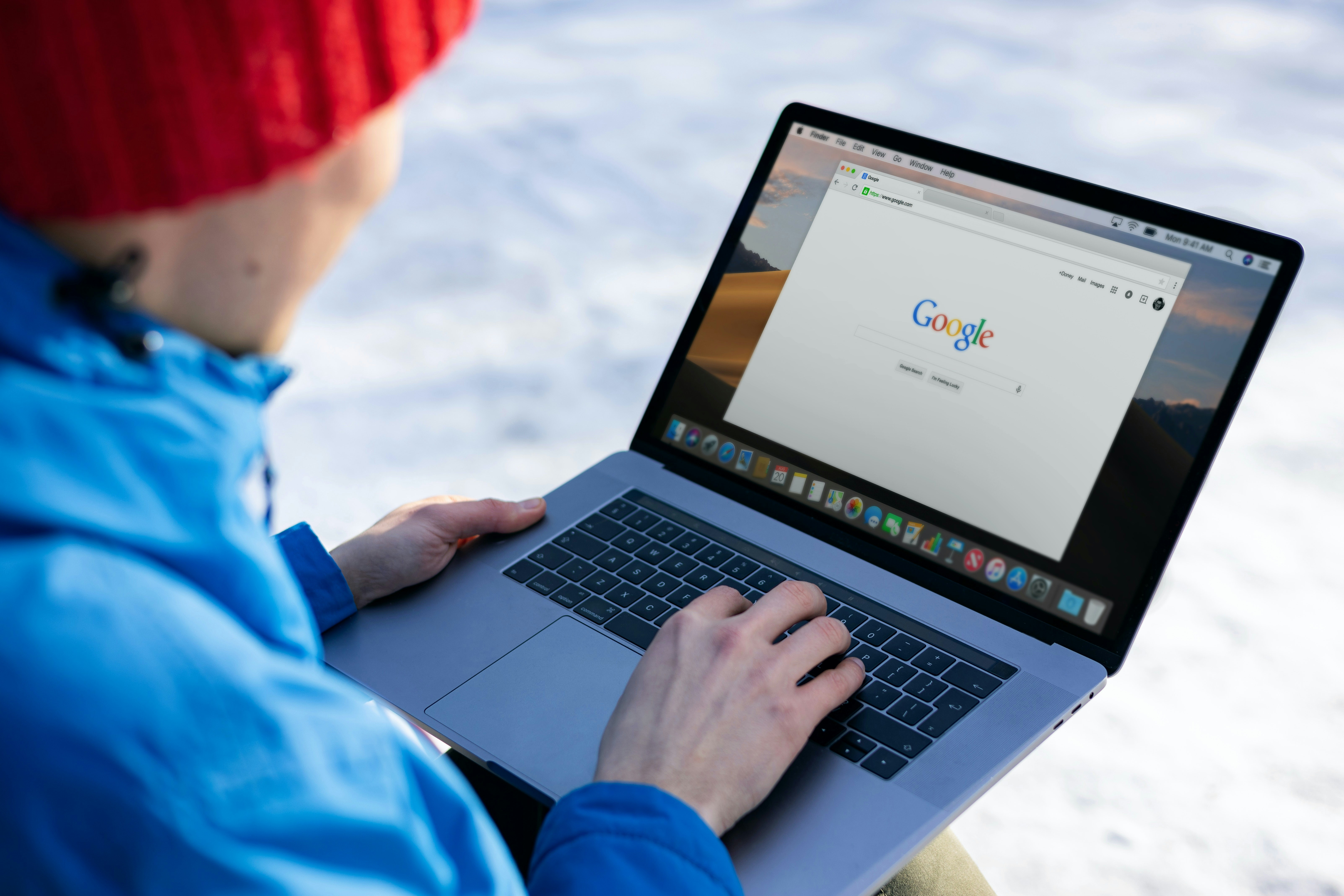 Persona vestita con indumenti invernali che sta al pc all'aperto in un luogo innevato. Lo schermo è sulla homepage di Google.