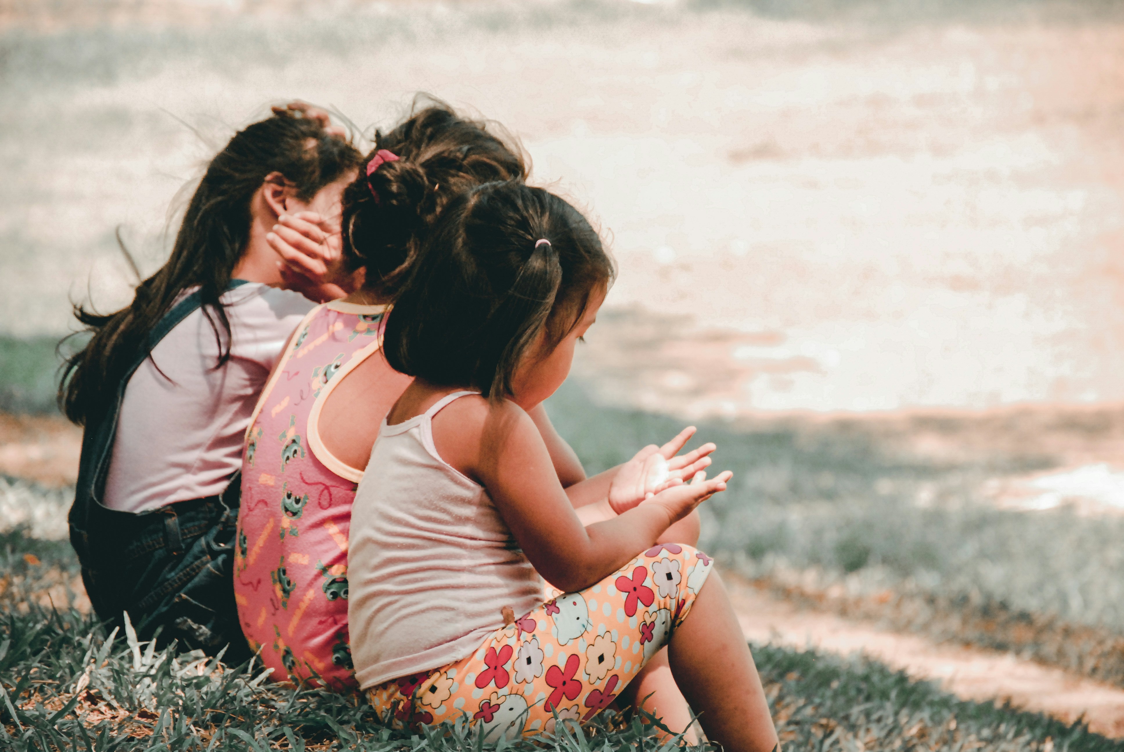 Immagine di bambini di spalle seduti per terra su un prato